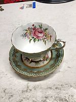 Teacup on saucer showing overall design, gold trim, floral centre, green border