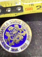 Front of round blue enamel Pennsylvania State University lapel pin showing emblem and lettering