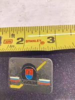 Front view showing SZTN hockey enamel lapel pin beside tape for scale