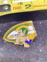 Front view of enamel pin showing mascot design and measuring tape for scale