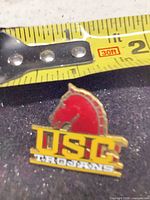 Front view of USC Trojans enamel lapel pin against tape measure showing size ~1 in