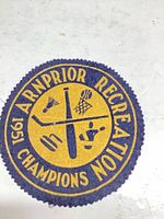 Front of round purple felt patch with yellow “1951 Arnprior Recreation Champions” text and sports icon design