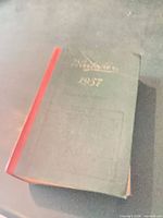 Front angled view of green hardcover book with red spine