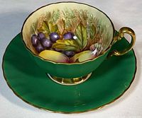 Teacup on saucer showing interior fruit painting and exterior color