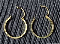Front view of both gold hoop earrings on dark fabric background