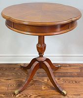 Full view of round pedestal side table showing top, pedestal, legs, brass feet