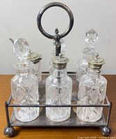 Front view of complete cruet set showing six bottles, stand, stoppers and silver-plate lids