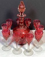 decanter with stopper surrounded by ten cordial glasses frontal view