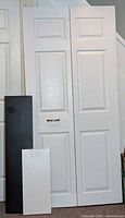 Front view of white bifold door with black and white shelves leaning against it