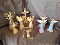 Full view of 7 angel and fairy figurines displayed with a cross and angel ornament box on grey fabric background.