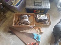 Photo showing Craftsman circular saw, battery booster, plastic toolbox, and three different handsaws with wooden and colored handles.
