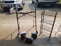 Wide view of Mobility and Homecare walker, manual massage accessory, Magic Bag thermotherapeutic pack, and metal rack on pavement.