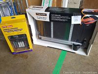 Fiskars 12" rotary paper trimmer in box and Staples printing calculator in retail box on floor.
