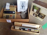 Photo showing cardboard box with Sharp calculator having paper receipt, 4x6 photo frame with white border, keychain and pen, decorative cubes boxed separately, and wooden cases holding ruler and pencils for lettering set.