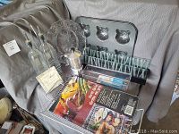 Full view of the lot showing all items including oil and vinegar set, grill grid, candle holder, glass decor plate, metal coffee maker, and metal mold pan.