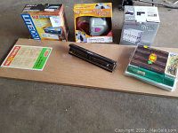 Photo of boxed LiteOn DVD drive, Skip Dr Automax disc repair system, wooden shelving board, hand stapler and a pack of CD cases