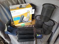 Photo showing unopened AT&T corded/cordless answering system box, blue two-hole puncher, 3 black mesh letter trays, and black mesh organizers.