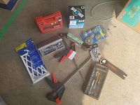 Photo of assorted tools including red reversible ratchet, socket sets, router bits, clamps, wirewheels, belt, and supports arranged on floor.