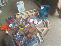 Lot items spread on floor including toolbox, power sander, bit sets, driver set, hand tools, levels, tool belt and accessories.