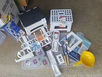 Two white plastic step stools, kitchen hooks, containers, paper towel holder, kitchen tools, picture frame pages and shelf support arranged on floor