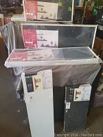 Photo of the 5 floating wall shelves in packaging, stacked on a covered table showing color options and box labels.