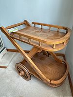 Overall view of solid wood two-tier serving cart with wheels and spindle rail accents