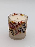 Front view showing painted leaf design on frosted glass jar with unused candle