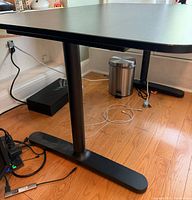 Side view of black desk showing one cylindrical leg and T-shaped foot