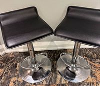 Two black faux leather bar stools front view showing seats and chrome bases