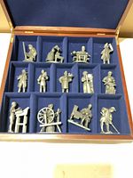 Open wooden case showing 13 pewter figurines in blue felt slots