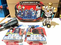 Group shot of all five items: Laser Battle game box, Fireworks Light Show projector, two Real Heroes packs, robot figure