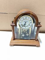 Front view showing dial, wooden arch top, glass front, brass pendulum