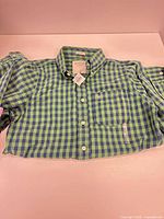 Full front view of shirt laid flat showing gingham pattern and long sleeves