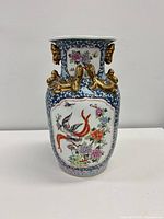 Front view of porcelain vase showing painted bird and floral panel, blue ground, gold dragon handles