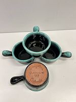 Four turquoise and black handled ramekins stacked showing interiors and one base