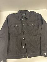 Front view of black denim jacket showing button-front and chest pockets