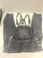 Full view of overalls laid flat front side showing straps and legs