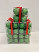 Stack of five clear boxes containing green glitter ornaments tied with red ribbon