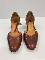 Front view of both brown leather ankle-strap pumps