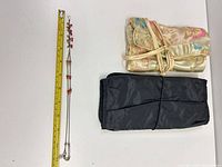 Closed gold satin jewelry roll and folded black Travelon organizer beside bead necklace and measuring tape