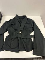 Full view of black blazer laid flat showing front, belt, single button