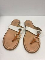 Top view of sandals showing white strap, tan footbed, gold ring detail