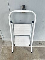Full view of white two-step folding foot stool against wall