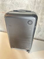 Front view of matte black Monos suitcase showing logo and exterior scuffs