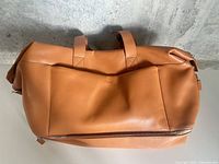 Front view of tan Monos vegan leather duffel bag showing exterior pocket and top handles