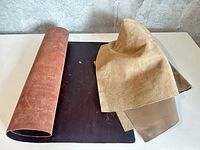 Three distinct leather pieces: rolled reddish suede sheet, flat dark brown hide, tan suede scraps