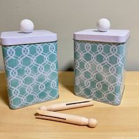 Two aqua teal geometric canisters with lids and two wooden clothespins on table