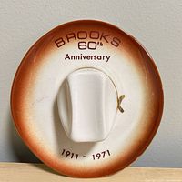 Front view of Brooks 60th Anniversary ashtray showing lettering, colour gradient, central snuffer