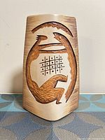 Front view showing carved fish, figure and grid motif on tan body