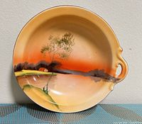 Front view of plate showing full hand-painted landscape scene and handle